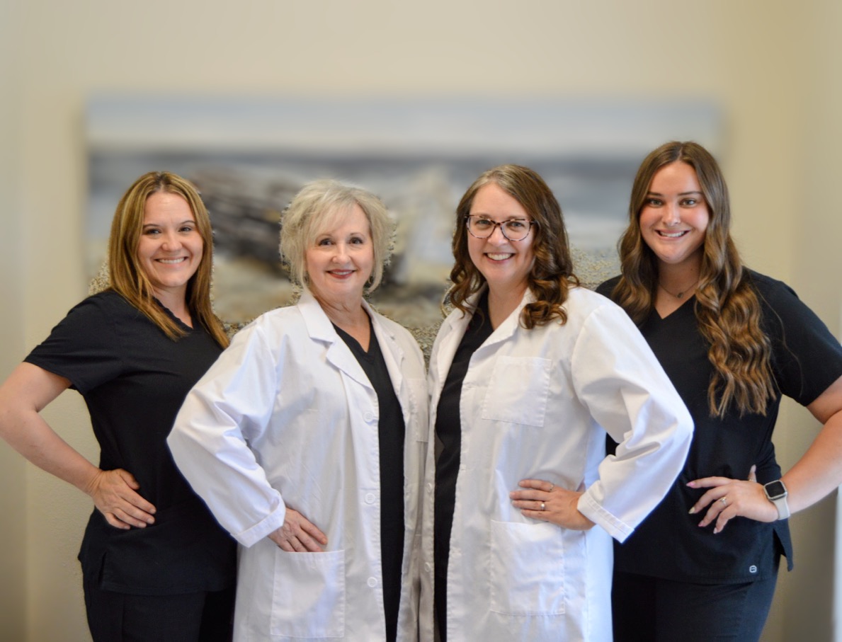 Four women smiling, two in white coats, two in black outfits.